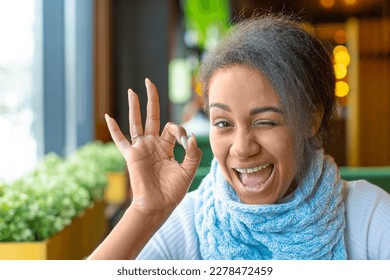 Portrait of an African American woman with a video call. She showing allright gesture. Close-up picture.