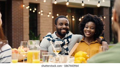 Portrait of African American young happy couple sitting in hugs at table outdoor and smiling to camera. beautiful woman and handsome man embracing at dinner picnic barbecue. Weekend at back yard. - Powered by Shutterstock