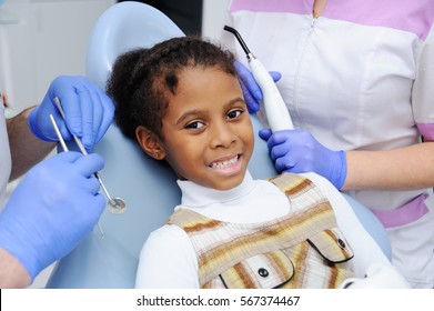 Portrait Of An African Baby Girl With Black Skin In The Dental Chair. The Dentist Examines The Mouth And Teeth Of A Young Child