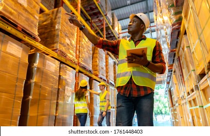 Portrait african black warehouse supervisor standing with digital tablet check stock in large warehouse distribution center with colleague worker in background. Business warehouse and logistic concept