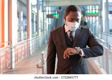 Portrait of African businessman with mask checking the time at the train station outdoors - Powered by Shutterstock