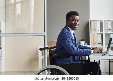 Portrait of African disabled businessman smiling at camera while typing on laptop computer at office - Powered by Shutterstock