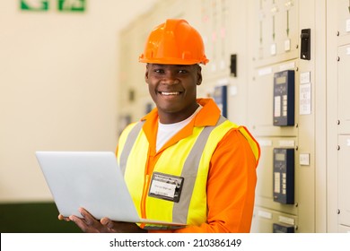 Portrait Of African Engineer Holding Laptop In Power Plant Control Room