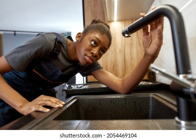 Portrait Of African Ethnicity Female Plumber Looking At Black Modern Faucet. Kitchen Amenities Maintenance. Breaking Gender Stereotypes Concept.