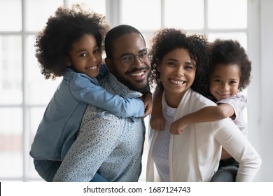 Portrait of African ethnicity parents piggy back son and daughter posing indoors. Pretty family looking at camera photo shoot in modern apartment at home, happy parenthood family services ad concept - Shutterstock ID 1687124743