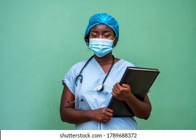 Portrait Of An African Health Care Provider Holding Patient Documents And Stethoscope Around Neck,wearing Face Mask And Head Gear For Protection