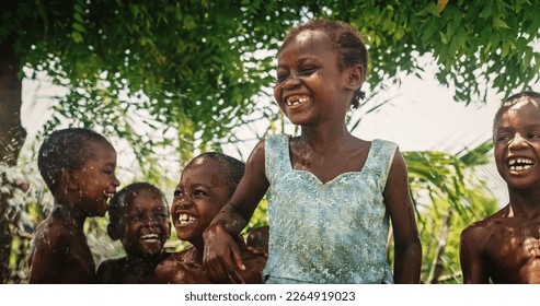 Portrait of an African Little Girl Jumping and Dancing with Other Kids Under Pouring Water. Happy and Innocent Black Children Playing and Enjoying the Blessing of Rain Water After Long Drought - Powered by Shutterstock