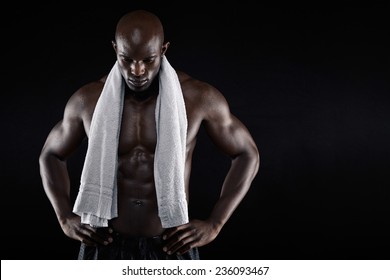 Portrait Of African Male Athlete After Workout Against Black Background. Shirtless Muscular Man With A Towel Looking Down With His Hands.