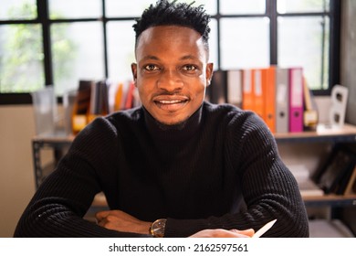 Portrait Of African Male Creative Smile And Look At Camera Sitting In The Office. Happy Positive Attitude Man In Minimal Style Meeting Team Or Customer On Video Conference.