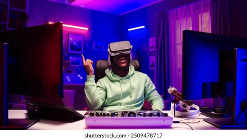 Portrait of African male wearing VR-glasses sits at table with DJ equipment. Satisfied handsome man uses gadgets in LED lighted room. - Powered by Shutterstock