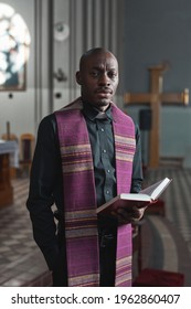 Portrait of African man in costume holding Bible and looking at camera while standing in the church during ceremony