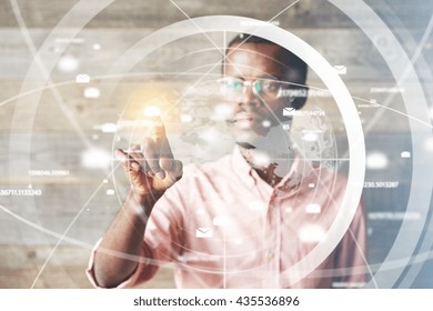 Portrait of African man in glasses, using digital device, pointing at icons on futuristic screen interface against high-tech interior, looking with serious concentrated expression. Selective focus