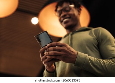 Portrait African Man With A Phone In His Hands Prints A Message In The Office. A Man With A Teleophone In His Hands, In A Room At Home. Online Shopping, Looking For Where To Go To Travel