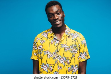 Portrait of african man wearing a Hawaiian style floral shirt and looking at camera. Young guy in summer style outfit against blue background. Tropical holiday concept.