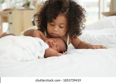 Portrait Of African Newborn Baby Sleeping On A White Bed. His Little Sister Kissing Infant Boy With Love. New Siblings Relationship In Bedroom At Home