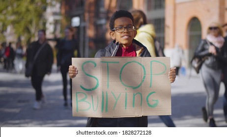 Portrait Of African Preteen Boy In Eyeglasses Standing Outdoors School Building With Stop Bullying Cardboard Sign. Bully, Aggressive Behavior And Offence Concept