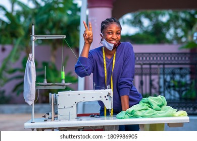 portrait of an African seamstress with two fingers up high and wearing face mask under chin-concept on woman entrepreneurship - Powered by Shutterstock