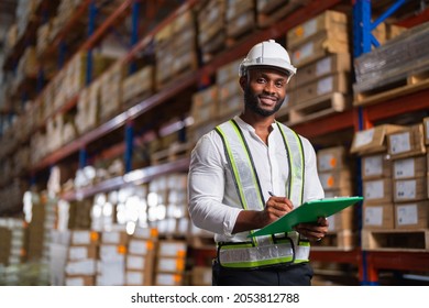 Portrait of an African warehouse manager holding a clipboard checking inventory in a large distribution center. - Shutterstock ID 2053812788