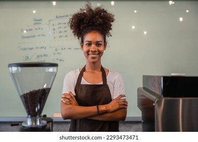 Portrait of African woman barista wearing apron standing smiling and arms crossed with looking at camera in the coffee shop. Confident young female worker waiting for service in cafes at restaurants. - Shutterstock ID 2293473471
