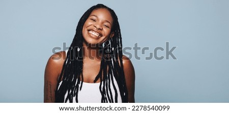 Portrait of an African woman with dreadlocks and body piercings smiling at the camera. Happy young woman feeling confident in her style. Fashionable woman standing against a studio background.