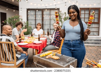 Portrait of African woman having fun, enjoy party outdoors in garden. Attractive diverse group of people having dinner, eating foods, celebrate weekend reunion gathered together at the dining table. - Powered by Shutterstock