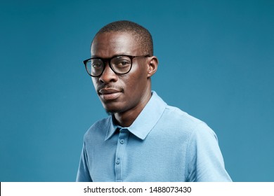 Portrait Of African Young Man Wearing Glasses And Blue Shirt Looking At Camera Isolated On Blue Background