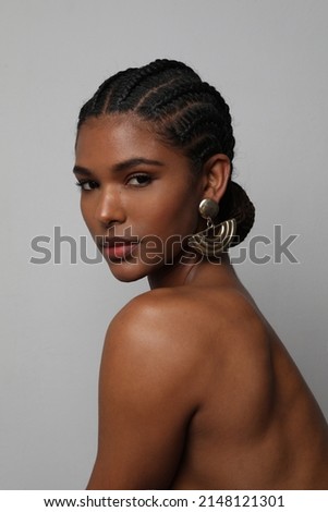 Portrait of African young woman with braids hairstyle posing on grey wall.