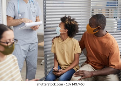 Portrait of African-American family wearing masks and looking at doctor while waiting in line at medical clinic