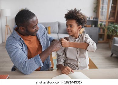 Portrait of African-American father fist bumping smiling son while doing homework together at home