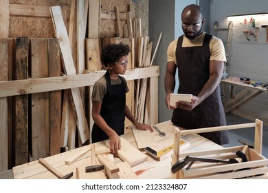 Portrait of African-American father teaching son carpentry while working together in woodworking shop - Powered by Shutterstock
