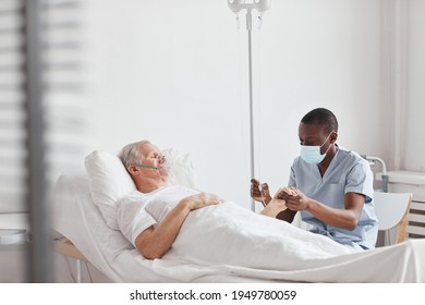 Portrait of African-American male nurse setting up IV drip while caring for senior man in hospital bed, copy space - Powered by Shutterstock