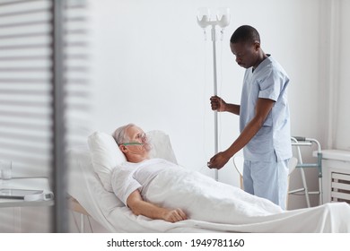 Portrait of African-American male nurse setting up IV drip while treating senior patient in hospital bed, copy space - Powered by Shutterstock