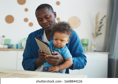 Portrait Of African-American Man Holding Crying Baby While Using Digital Tablet In Home Interior, Copy Space