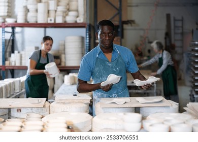 Portrait of african-american man potter holding new decorative plate, smiling and looking at camera. - Powered by Shutterstock