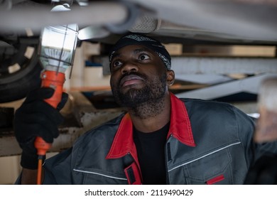 Portrait of African-American mechanic inspecting car on vehicle lift in auto repair shop, copy space
