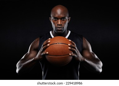 Portrait Of Afro American Male Basketball Player With A Ball Over Black Background. Fit Young Man In Sportswear Holding Basketball.