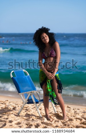 Portrait of an Afro Brazilian Pretty Girl Onix Skin Serious Looking Curly Hair Style Wear Swimsuit, Standing w. Brazilian Flag on Waist in a Warm Atlantic Ocean of Rio de Janeiro Impressive Landscapes