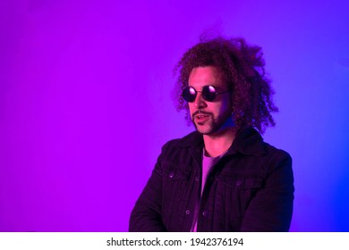 Portrait Of An Afro-American Hipster Man, Afro Hair, In The Style Of The 80s And 90s, Steampunk Glasses, Blue And Purple Neon Lights. Smiling And Laughing.