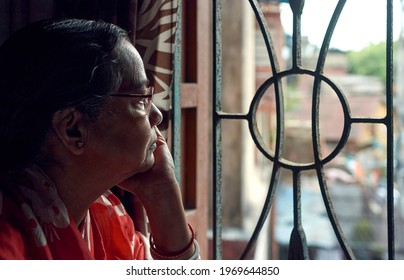 Portrait of an aged Indian (Bengali ethnicity) looking outside from her room window. As precaution from covid-19 pandemic, she is staying at home.