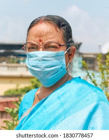 Portrait of an aged Indian woman, wearing traditional blue coloured Indian sari and surgical face mask, for protection from coronavirus infection. 