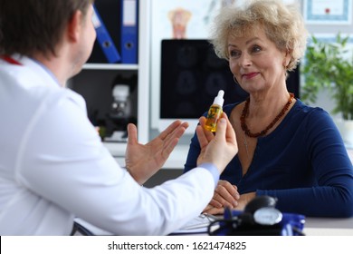 Portrait of aged senior female consulting with doctor. Therapeutic in medical gown advising cannabinoid oil to patient. Practitioner holding bottle with cannabis leaf sign