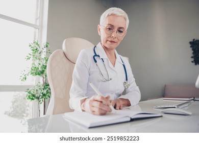 Portrait of aged woman professional doctor pen write notebook wear white coat workplace office indoors - Powered by Shutterstock