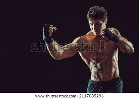 Portrait of aggressive boxer training and practicing uppercut. Isolated on black studio background. Concept of sport, healthy lifestyle. 