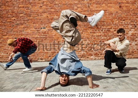 Portrait of all male breakdance team doing head stand against brick wall outdoors in sunlight ストックフォト © 