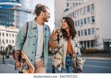 Portrait of alternative young trendy tourist couple walking on urban city street with skateboards in hands and smiling at each other. Hipster visitors talking and walking on city street downtown. - Powered by Shutterstock