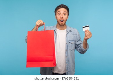 Portrait of amazed handsome man in stylish denim shirt holding credit card and shopping bags with blank space for advertise text, looking with shocked expression. indoor studio shot, blue background - Shutterstock ID 1765304531
