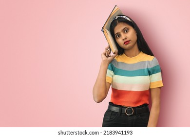 Portrait of an amazed indian asian girl student with big eyes posing isolated holding book on one side of her head and looking directly to camera with copy space.