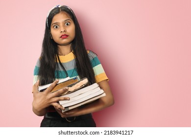 Portrait of a amazed indian asian girl student with open mouth and big eyes posing isolated holding a lot of books and shocked by seeing exam syllabus. Education concept