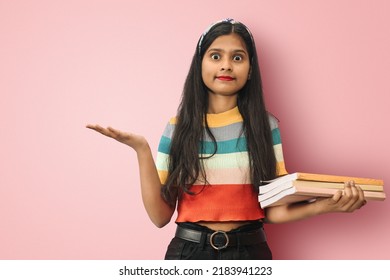 Portrait of a amazed indian asian girl student posing isolated holding copyspace on the palm and books on the other hand with big eyes like recommending something.