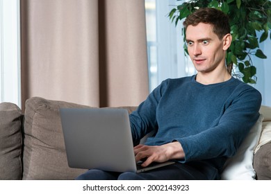 Portrait Of Amazed Surprised Shocked Guy, Young Man Using Laptop, Typing On Computer With Excited Face, Sitting At Home On Sofa Or Couch In Living Room. Wow, Can't Believe, Winner Win